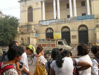 A group stands before the old SBI building, learning about its history, from being part of Begum Samru's palace to housing the Delhi and London Bank.