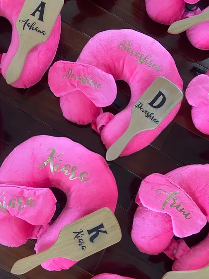 Birthday favors for the little girlies. These personalized travel sets include a bright pink neck pillow, an eye mask, and a custom hairbrush, all with their names in gold.