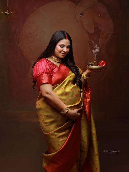 A standing portrait holding a diya, a classic pose in traditional maternity photography. The image is filled with warmth, grace, and cultural symbolism.
