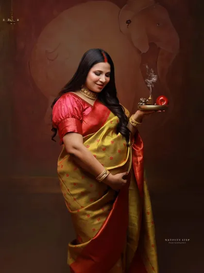 A standing portrait holding a diya, a classic pose in traditional maternity photography. The image is filled with warmth, grace, and cultural symbolism.