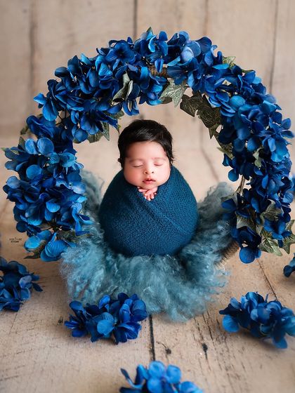 A beautiful baby boy surrounded by a wreath of deep blue flowers. This newborn portrait showcases a more vibrant color palette while keeping the focus on the sleeping baby.