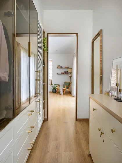 This open-shelf walk-in wardrobe is a highlight of the room, featuring wood and glass shutters that offer a glimpse into the space beyond.