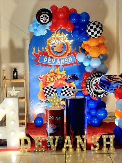 A Hot Wheels themed 4th birthday party with a custom backdrop, checkered flag details, and a balloon arrangement in bold red, blue, and orange. The marquee number '4' and personalized name add a special touch.