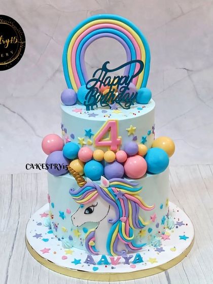 A magical two-tier unicorn cake for a fourth birthday. This pineapple cake features a large 2D unicorn, a rainbow topper, and is decorated with colorful fondant balls and stars.