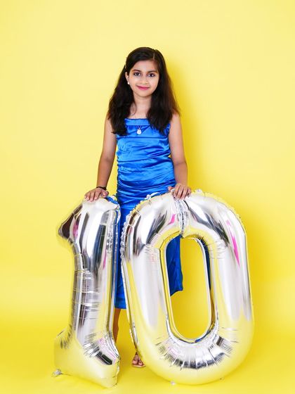A proud 10-year-old stands with her giant birthday balloons, celebrating a big milestone in a vibrant studio setting.