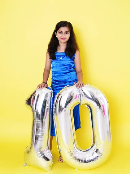 A proud 10-year-old stands with her giant birthday balloons, celebrating a big milestone in a vibrant studio setting.