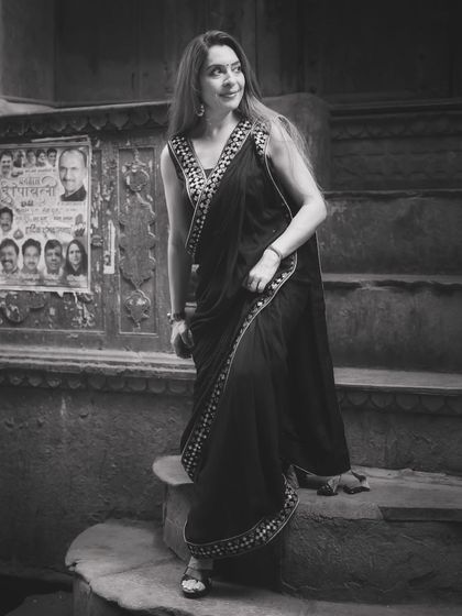 A classic black and white portrait that emphasizes the timeless elegance of the saree. The old movie posters in the background add a touch of nostalgia and character to the shot.
