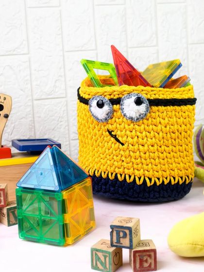 A bright yellow, Minion-inspired crochet basket filled with colorful magnetic tiles. This playful shot is perfect for showcasing kids' room decor and storage solutions.