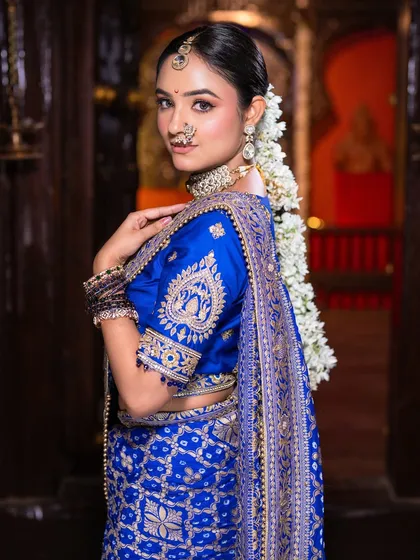 A side profile showcasing the traditional gajra hairstyle. The floral arrangement is a beautiful complement to the clean makeup and royal blue saree.