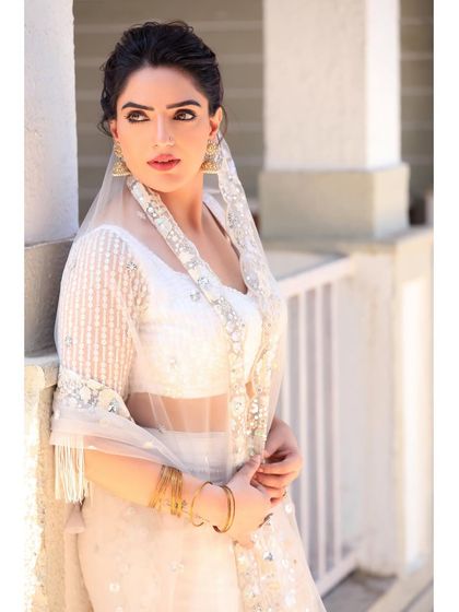 A three-quarter portrait featuring a sheer, embroidered dupatta. The layering of fabrics and the model's serene expression create a look of timeless elegance.