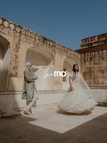 A stylish pre-wedding portrait in Jaipur, using the palace's weathered walls and strong shadows to create a modern, editorial feel. The bride's flowing lehenga adds a touch of dynamic movement to the scene.