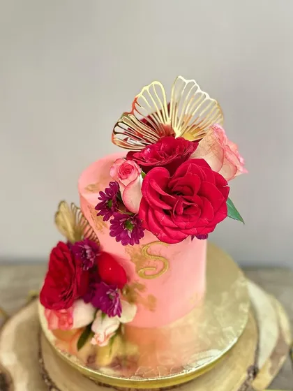 A top-down view of the vibrant pink floral cake, showing the arrangement of fresh flowers and the gold fan accents.