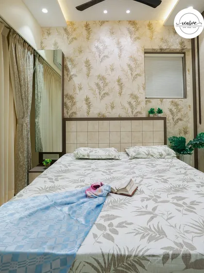 A cozy bedroom with a neutral, leafy wallpaper and a comfortable, well-styled bed.