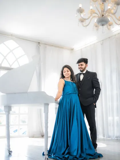 A full-length portrait of the couple standing by a grand white piano in an elegant, all-white room, adding a touch of classic romance.