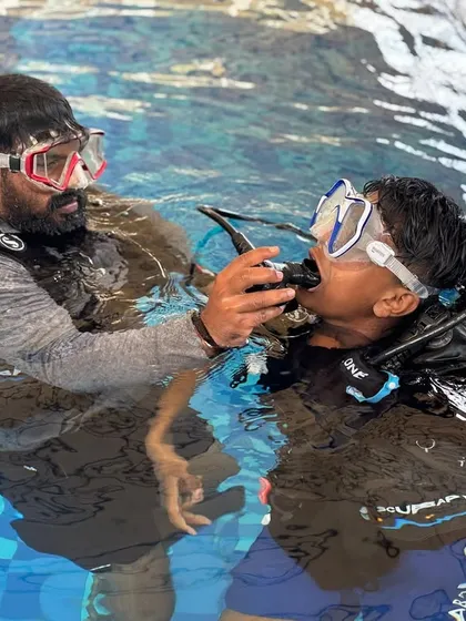An instructor carefully adjusts a student's scuba gear in the water, demonstrating our commitment to hands-on teaching and safety.
