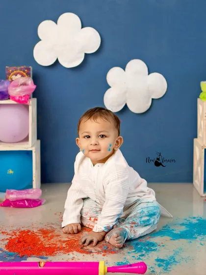 A moment of quiet curiosity amidst the colorful chaos of a Holi setup. The contrast between the calm expression and messy clothes tells a great story.