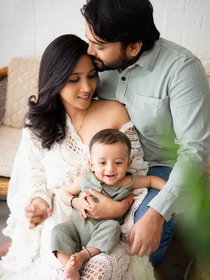 A loving family portrait, with dad kissing mom's forehead as they hold their smiling baby.