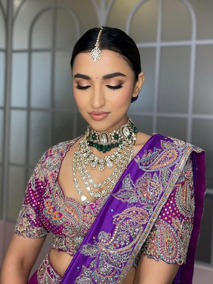 A close-up with eyes closed, showing the expertly blended, neutral-toned eyeshadow. This choice of eye makeup balances the vibrant purple of the lehenga, creating a sophisticated and modern look.