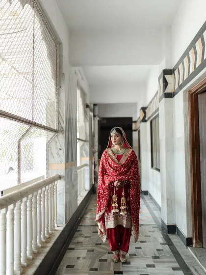 A full-length shot in a beautiful marble corridor. The simplicity of the background makes her traditional red Punjabi suit and jewelry stand out.
