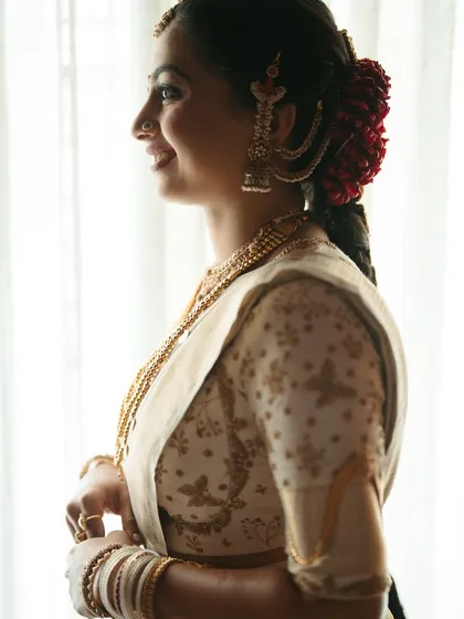 A side profile of a bride in her off-white Kanchipuram saree, showing the delicate floral embroidery on the blouse and her traditional bridal hairstyle with fresh flowers.