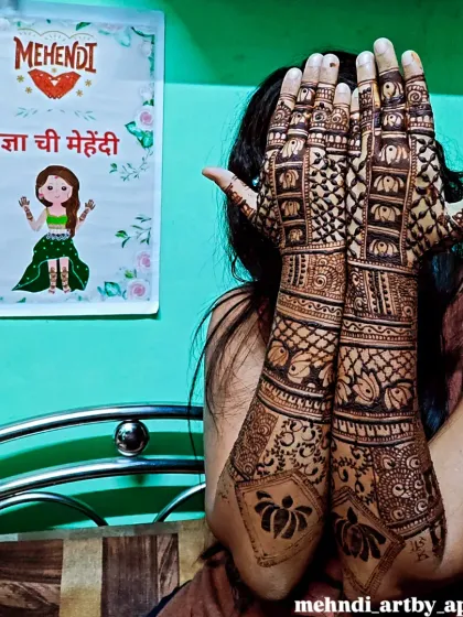 A fun pose showing off the full extent of this bridal mehendi. The design is packed with details, including rows of elephants and intricate checkerboard patterns that cover the arms.