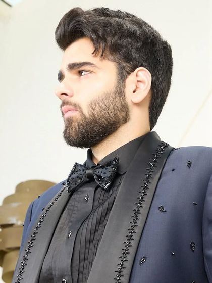 A close-up on the details of the navy blue tuxedo, showing the texture of the fabric and the intricate beadwork on the lapel and bow tie.