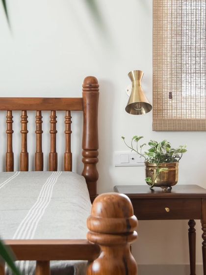 The guest bedroom features a custom-made wooden bed with classic turned posts. A brass wall sconce and a woven blind add layers of texture and warmth to the serene space.