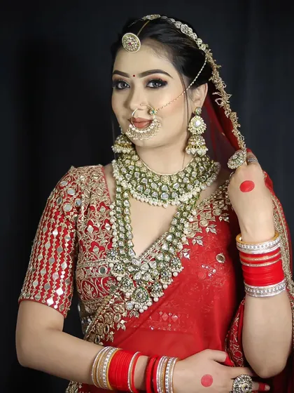 A confident pose from a bride in a red and gold ensemble. The makeup is bold yet elegant, with a focus on creating a radiant complexion that lasts through all the wedding ceremonies.