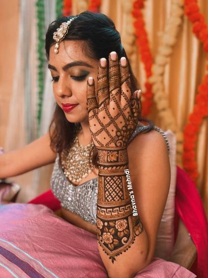 A bride looking elegant while showcasing her detailed back hand mehndi. The design features a beautiful floral band and a classic grid pattern, perfect for a sophisticated bridal look.