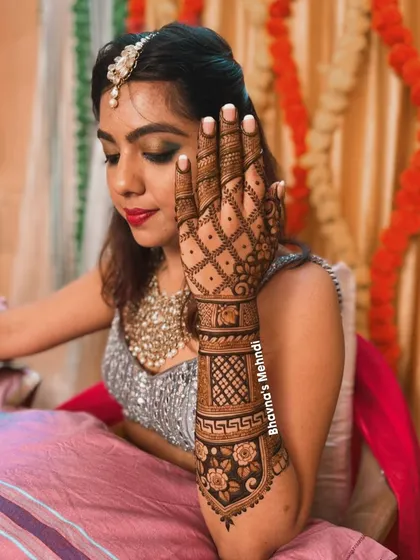A bride looking elegant while showcasing her detailed back hand mehndi. The design features a beautiful floral band and a classic grid pattern, perfect for a sophisticated bridal look.