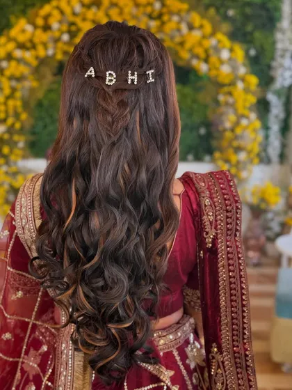 A personalized touch for the bride. This beautiful hairstyle features soft waves and a custom hair clip with the groom's name, adding a sweet and romantic detail to her look.