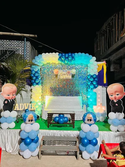 A full stage setup for a Boss Baby themed birthday. The decor features character cutouts on balloon pillars, a sequin backdrop, and a balloon arch.