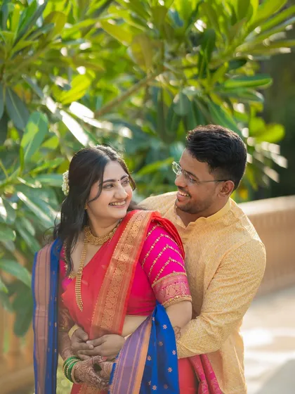 A candid and joyful moment between Jagruti and Shubham. The natural, leafy background complements their vibrant traditional outfits.