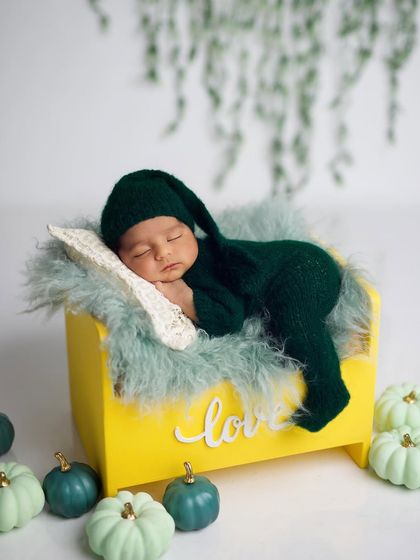 A sleeping newborn in a green pixie-style outfit, resting on a bright yellow bed. The contrasting colors and whimsical props create a playful and unique portrait.