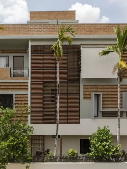 A full view of the Ananda residence in Hyderabad. The design combines renovated sections with new extensions, using a facade of striated earth blocks and wooden louvers to create a modern yet earthy aesthetic.