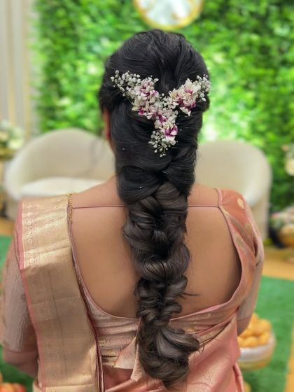 A close up of a thick pull-through braid, adorned with a V-shaped floral arrangement of baby's breath and other small flowers.