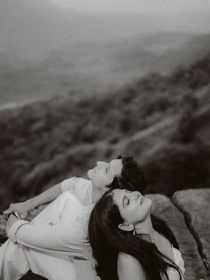 A timeless black and white photograph of a couple relaxing on a cliff edge. This candid moment, with the forest valley below, feels both peaceful and deeply romantic.