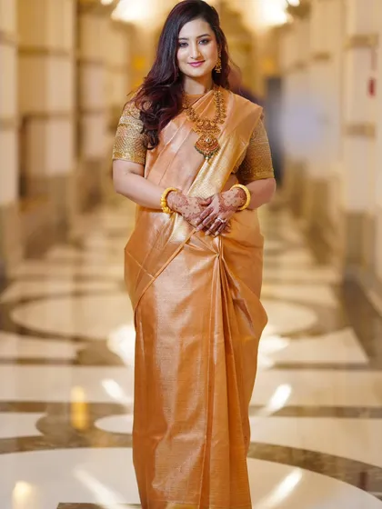 A full-length portrait showcasing the bride's graceful posture and the beautiful drape of her golden silk saree. She exudes confidence and elegance.