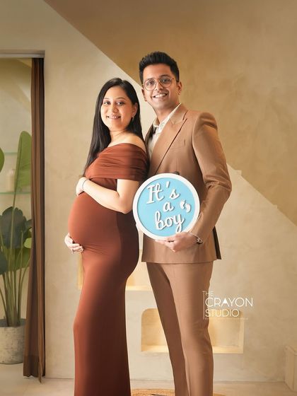 A classic and elegant gender reveal. The couple holds up a sign announcing "It's a boy" with proud and happy smiles in the studio.