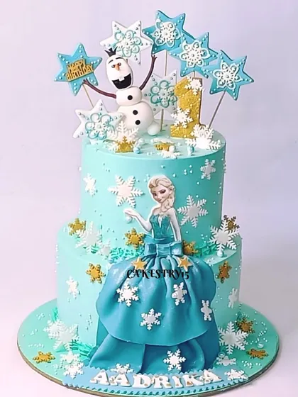 A beautiful two-tier Frozen-themed cake. This design features a fondant Elsa, Olaf, and is decorated with edible snowflakes and stars for a magical winter celebration.