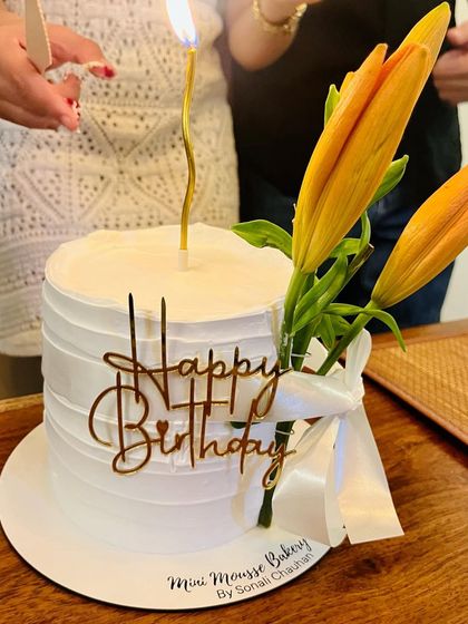 A beautiful moment captured as the birthday candle is lit. This minimalist white cake is adorned with fresh yellow lilies and a 'Happy Birthday' topper.