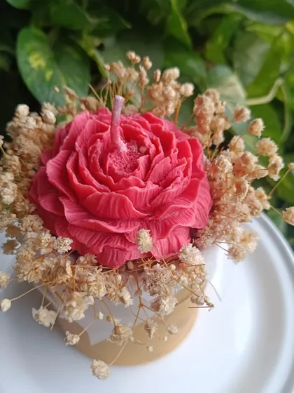A wax flower bouquet featuring a large peony-style candle surrounded by dried baby's breath.