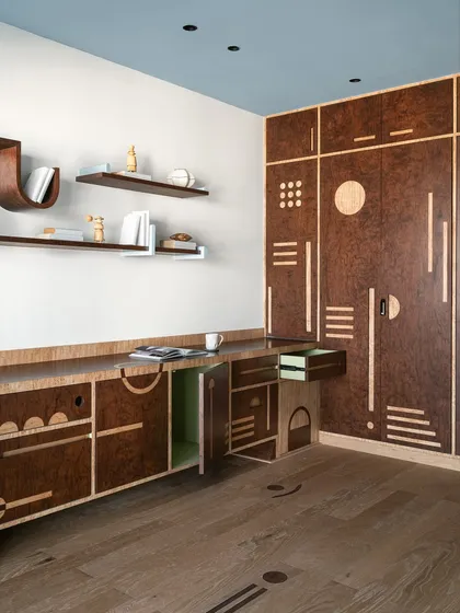 Storage should never be boring. For this multipurpose room, we designed a full-wall unit in rich burl veneer with intricate geometric inlays. The design combines different shutter types and playful motifs, with a surprise pop of mint green inside, turning a practical piece into a visual delight.