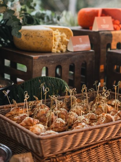 A rustic basket filled with savory pastries is a key feature of this farm-to-table inspired spread. Large wheels of cheese and other bites are displayed on wooden crates, enhancing the natural aesthetic.