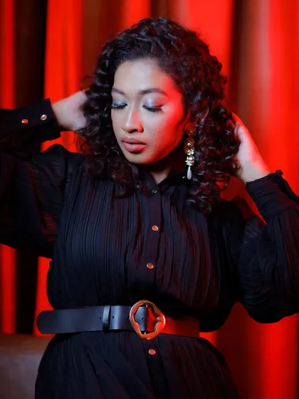 A close-up of the final look on curly hair, showcasing the soft glam makeup under dramatic red lighting.