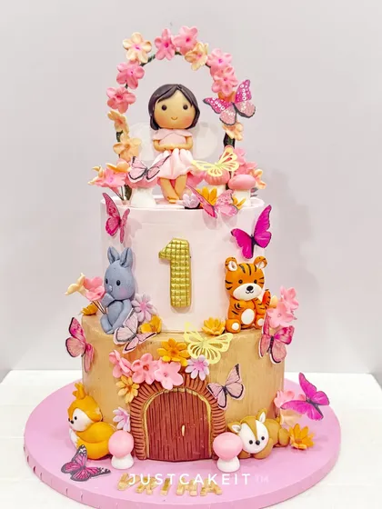 A magical woodland fairy cake for a first birthday. The design features a fairy, cute animals, and a floral arch, creating an enchanted forest scene.