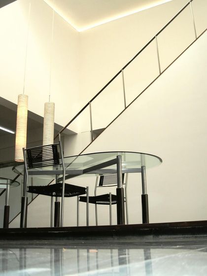 A meeting area at the Zanav Home Studio, seen from a low angle that emphasizes the polished floor and the light, transparent quality of the furniture and railing. The space is designed to feel open and uncluttered.
