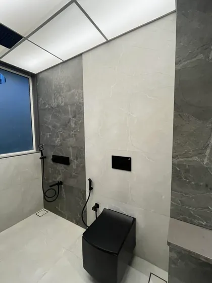 Another view of the Sanpada bathroom, highlighting the combination of dark and light grey tiles. The wall-mounted toilet and concealed cistern help create a clean, uncluttered floor space.