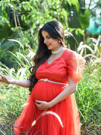 A soft and gentle outdoor portrait of a mom-to-be in a red gown, surrounded by tall, delicate grasses.