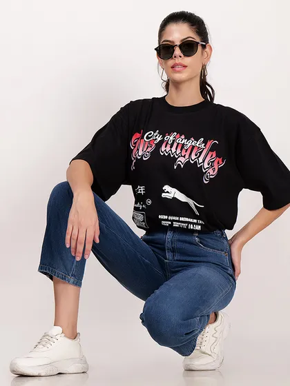 A model in a crouching pose wearing a black graphic t-shirt and sunglasses, creating a cool, urban look for a streetwear brand.